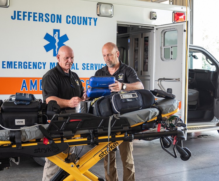 Two members of Jefferson County EMS stand in front of a stretcher by an ambulance.