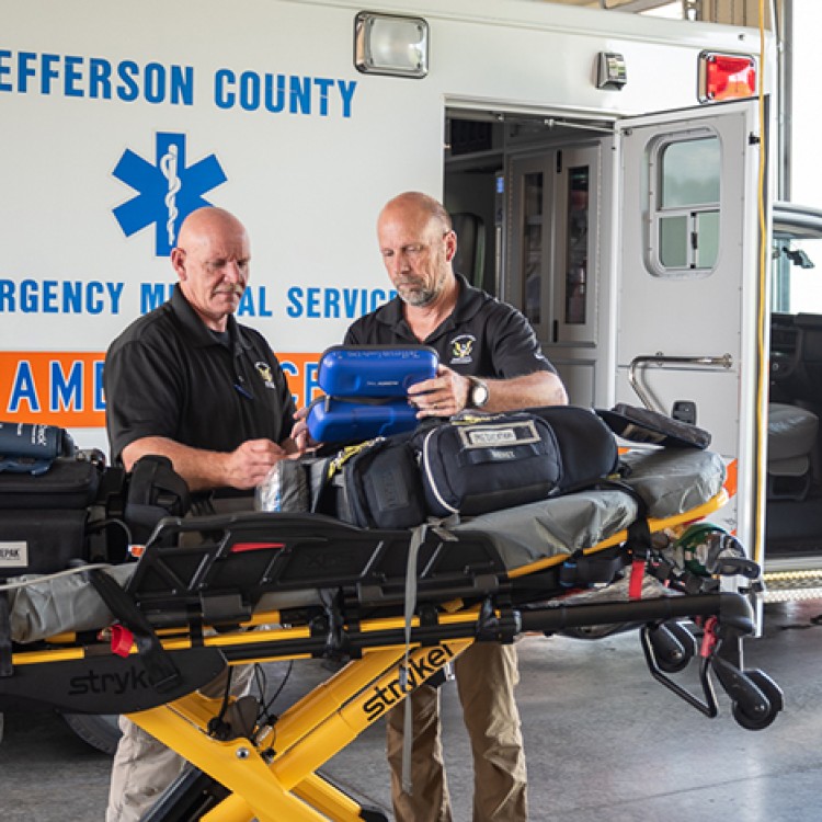 Two members of Jefferson County EMS stand in front of a stretcher by an ambulance.