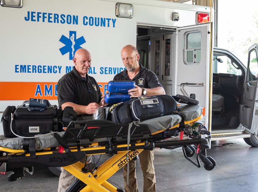 Two members of Jefferson County EMS stand in front of a stretcher by an ambulance.