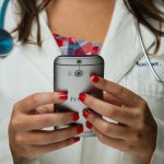 A doctor in a white coat holds a cell phone.